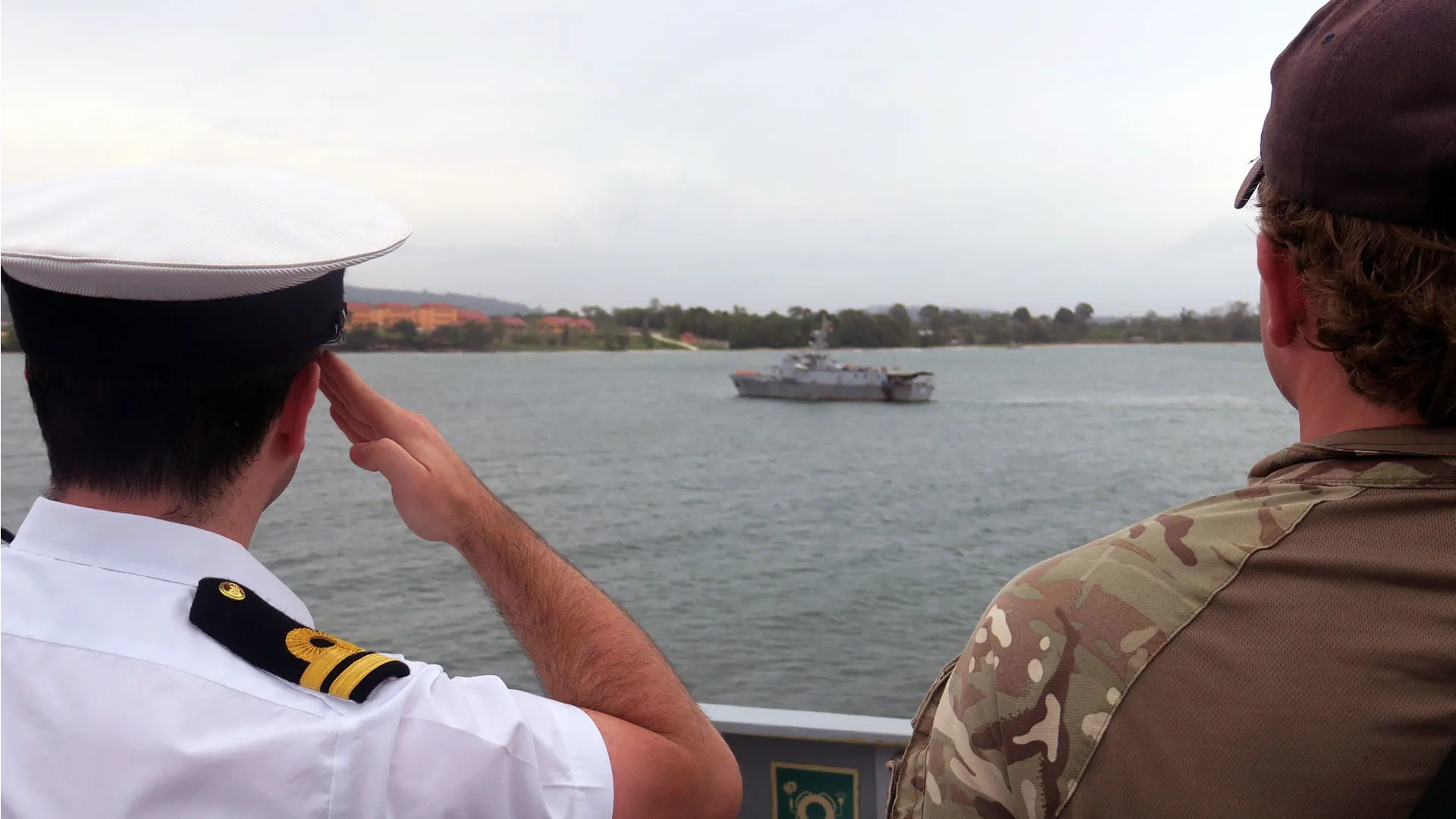 A junior officer salutes as HMS Tamar passes a Cambodian warship on entry into port