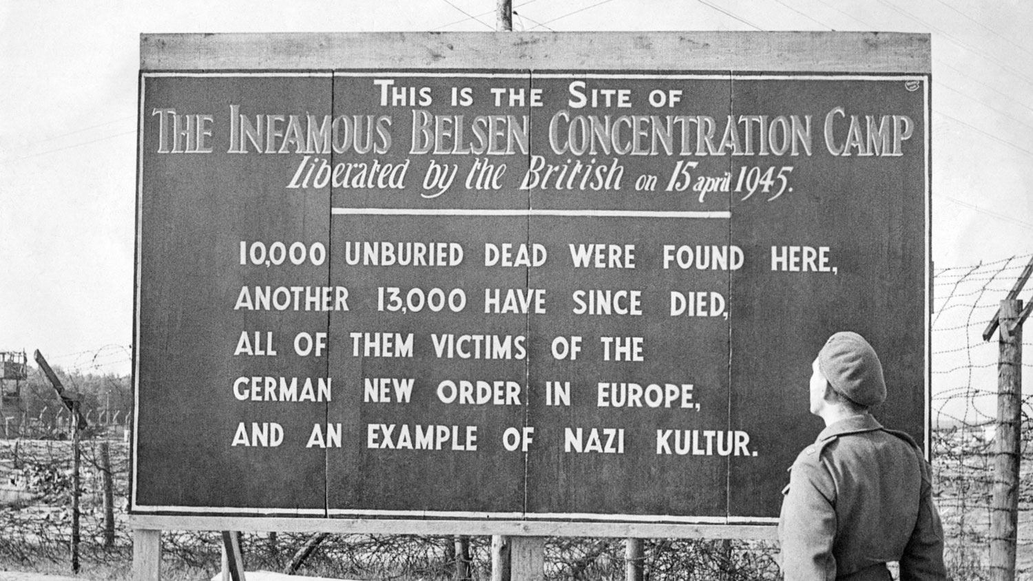 A British soldier stands by a sign posted at the site of the Belsen Concentration Camp, 1945