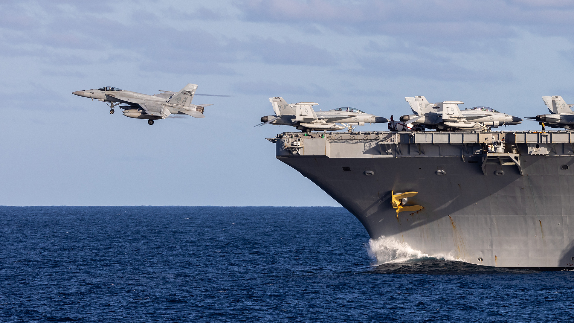A single-seat FA-18E Super Hornet passes several two-seat F variants at speed as it takes off from USS George Washington