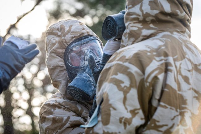 A member of 1st Battalion Scots Guards, helps his comrade by decontaminating his respirator during 