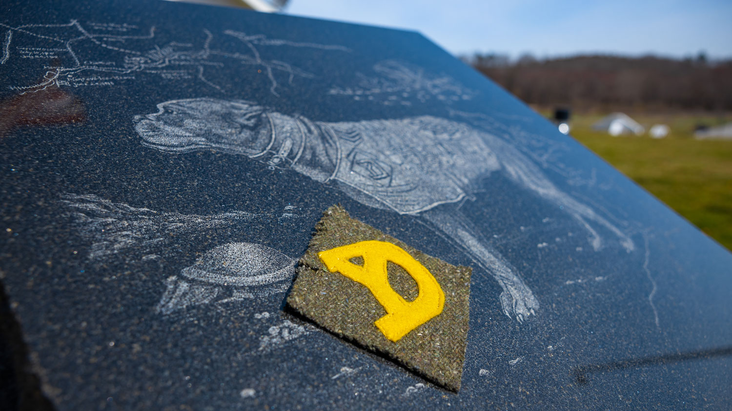 A WW1-era shoulder sleeve insignia of the 26th Division is placed beside an artist's depiction of Sgt Stubby on top of a monument outside the Newtown Military Working Dog Facility in Connecticut in April 2023 CREDIT US Army