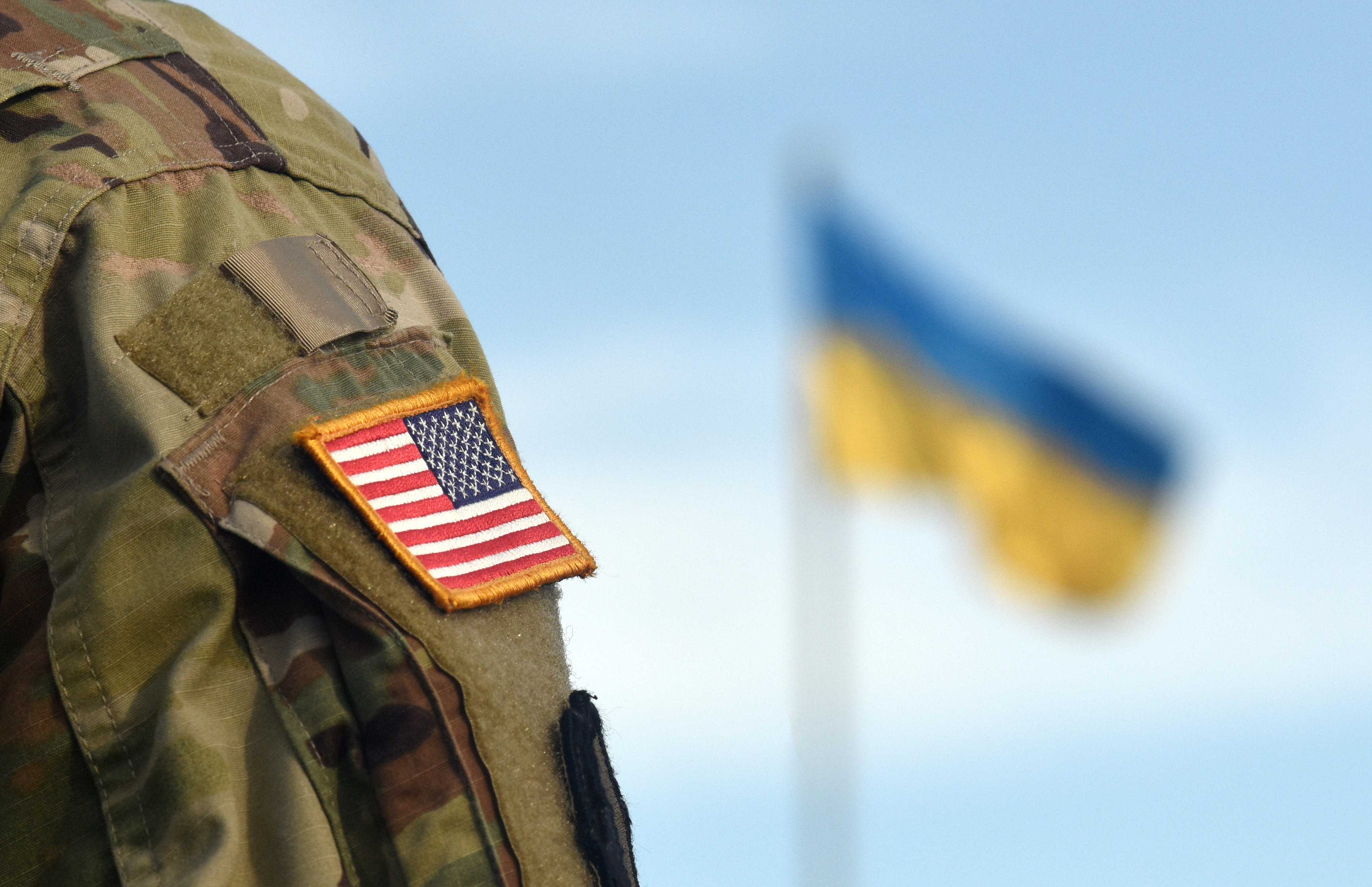 Anonymous member of the US Armed Forces with a Ukrainian flag flying in the background 
