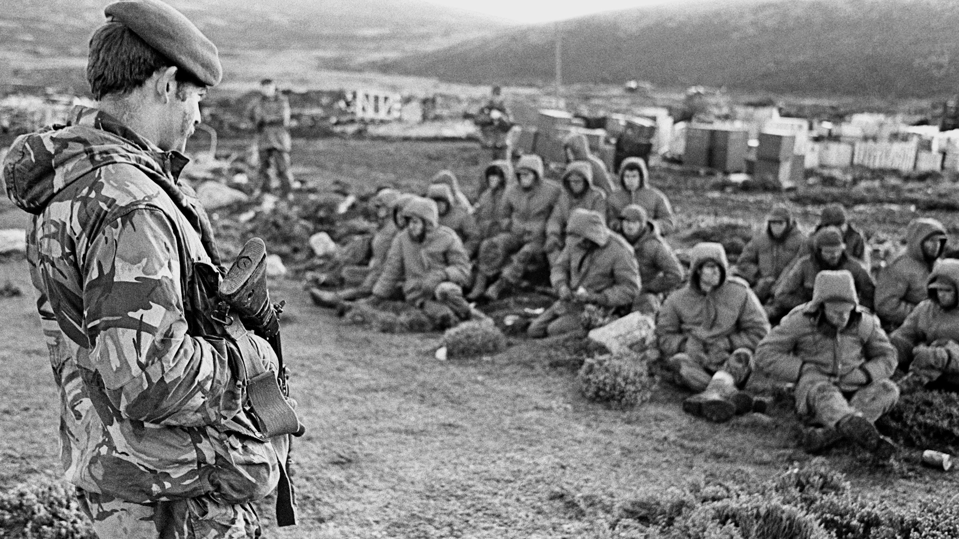 Argentinian soldiers captured at Goose Green are guarded by a British Royal Marine as they await transit out of the area 020682 CREDIT PA Alamy Stock Photo.jpg