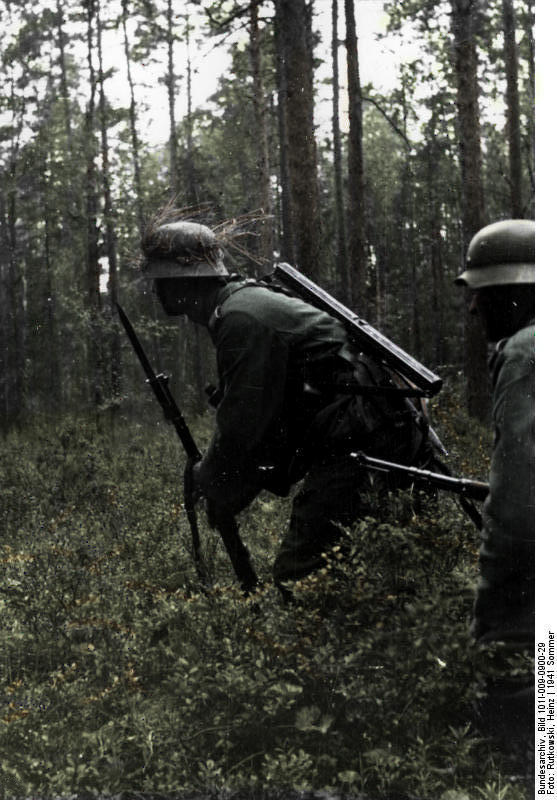 Two German soldiers (including a soldier with a bayonet attached) in a crouched position in a wooded area. Picture: Ruffneck88 / Bundesarchiv.