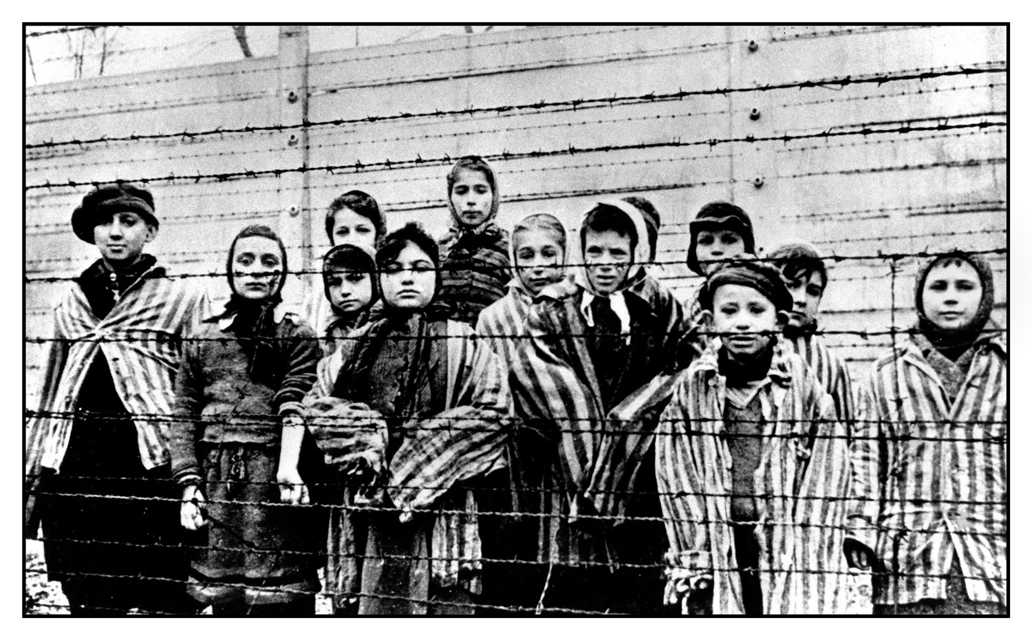 Child prisoners wearing striped uniforms stare out from behind a barbed wire fence in notorious WW2 Nazi death-camp Auschwitz Southern Poland Holocaust (Picture: Shawshots / Alamy Stock Photo).