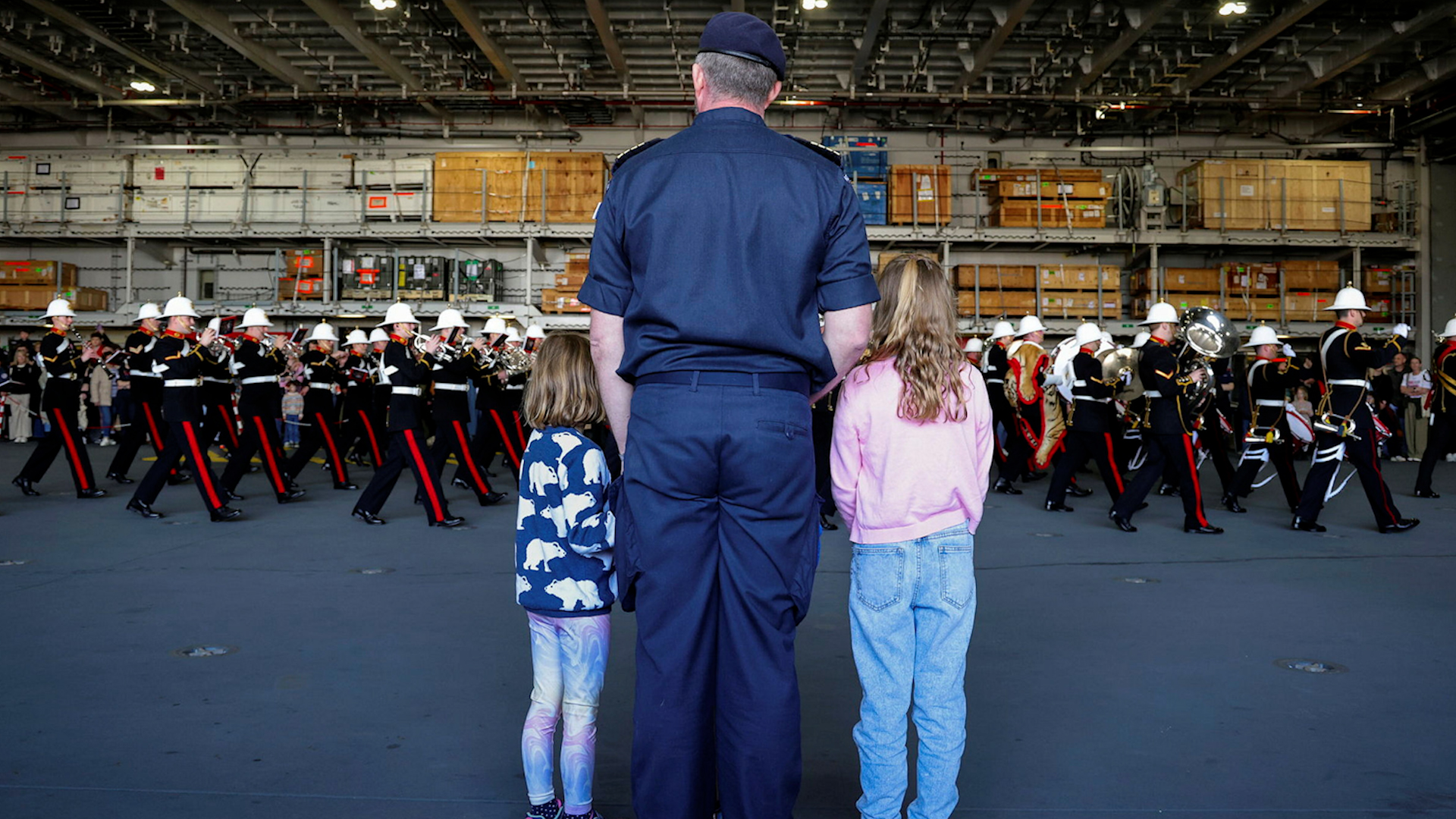 A crew member and his children watch the Marine Band perform on board HMS Prince of Wales