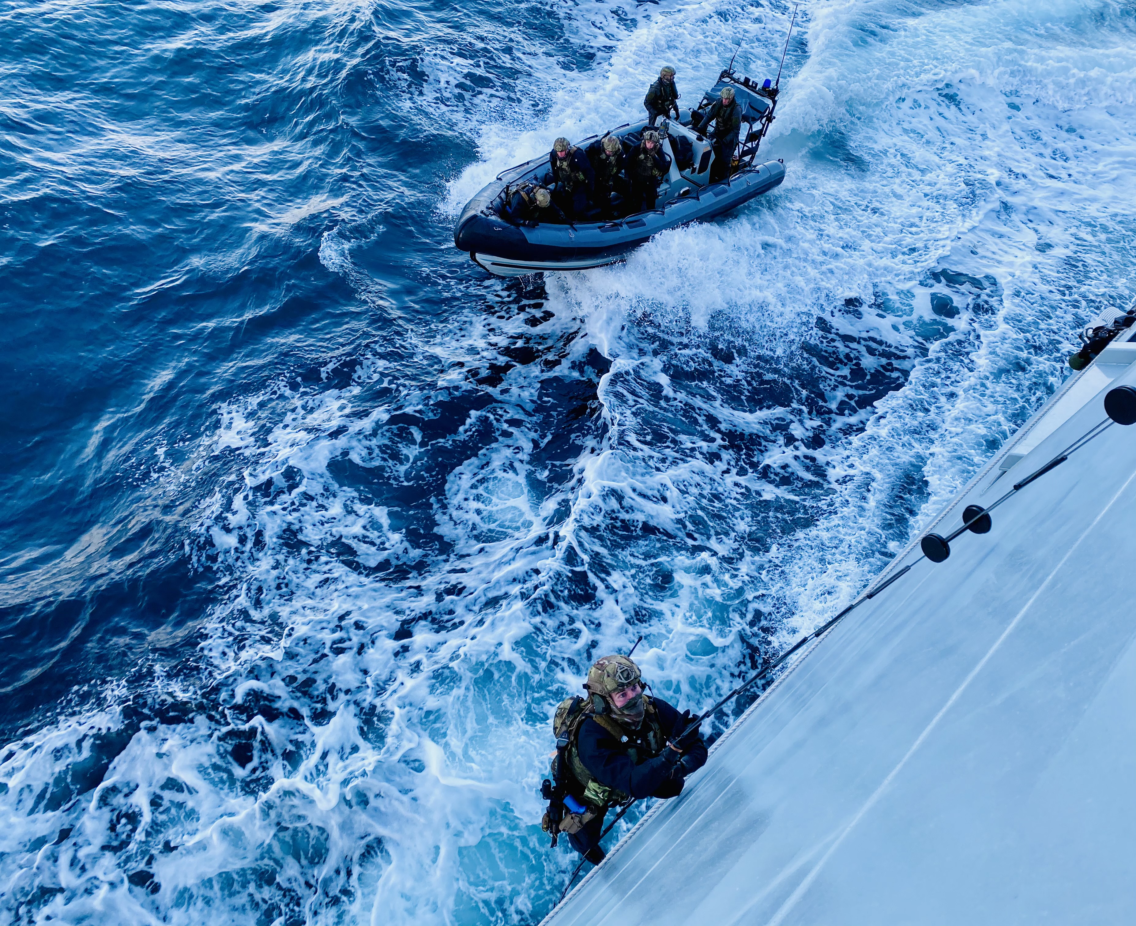 A marine begins scaling the sides of HMS Tamar.