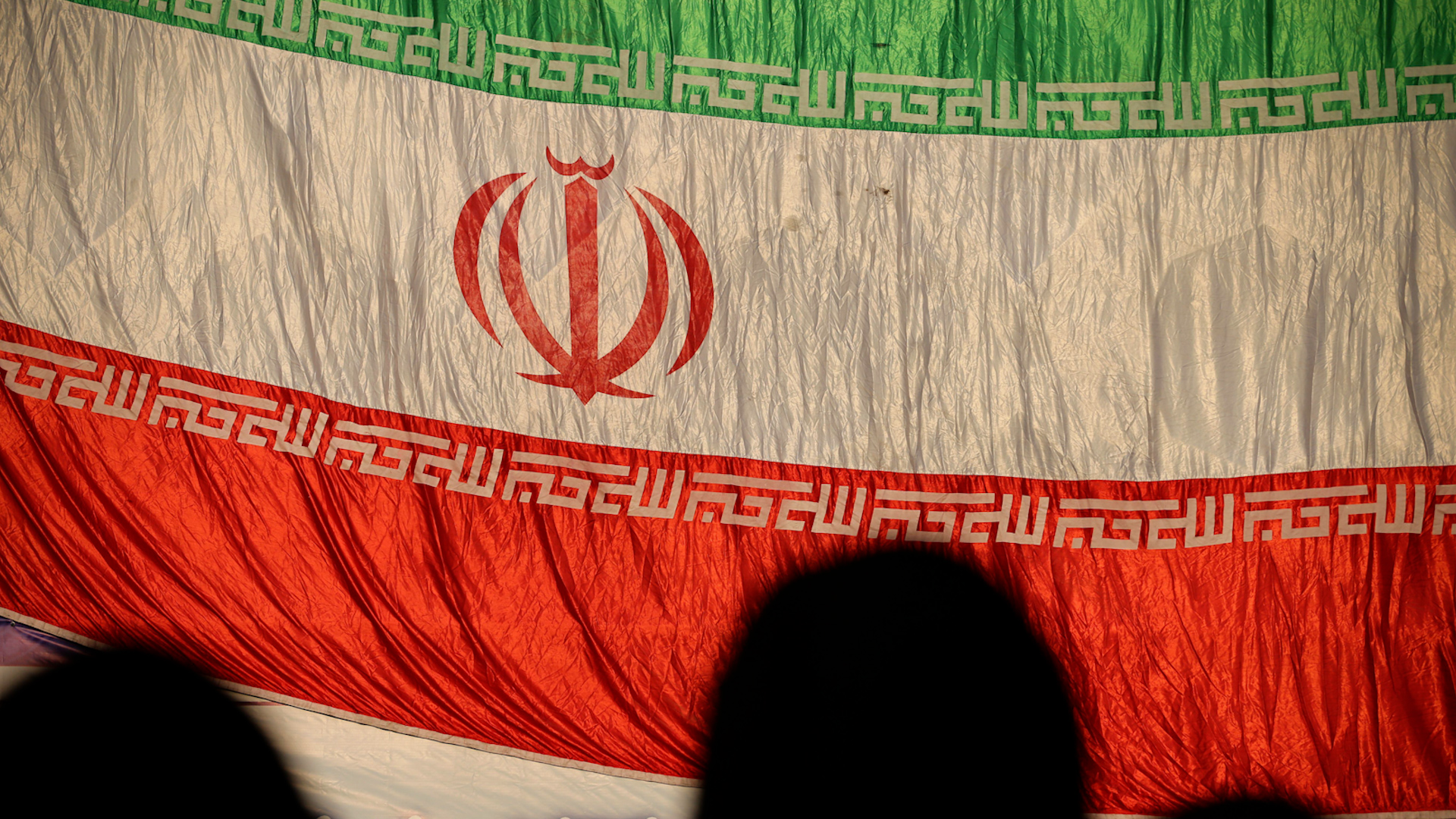 Generic photo of three veiled women silhouetted in front of the Iranian flag during a rally in Tehran (Picture: Zuma Press, Inc./Alamy Stock Photo).