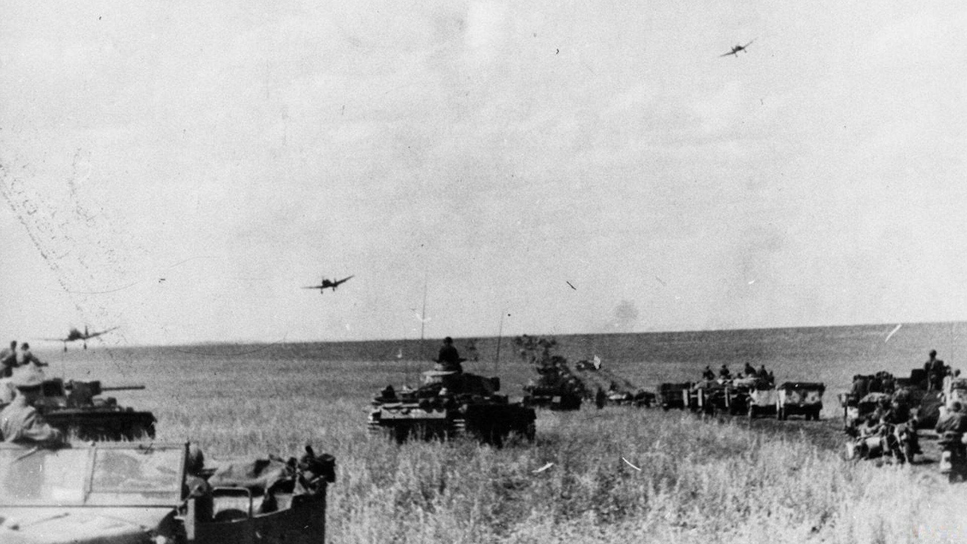 Junkers Ju 87 Stuka dive bombers returning to their base fly low over an advancing German column of Panzer III