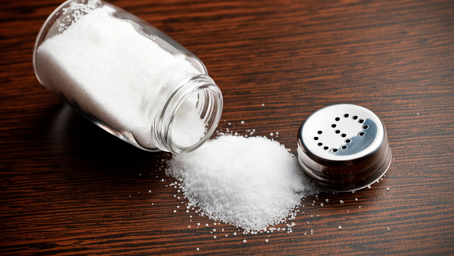 Image ID D7A435 salt sprinkled on a wooden table with the salt shaker lying next to it CREDIT HERA FOOD Alamy Stock Photo EXP 231124