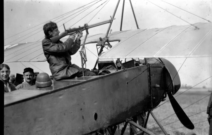 A pilot sitting on a French Morane-Saulnier L with a forward-firing gun, attempting to mount it to the plane