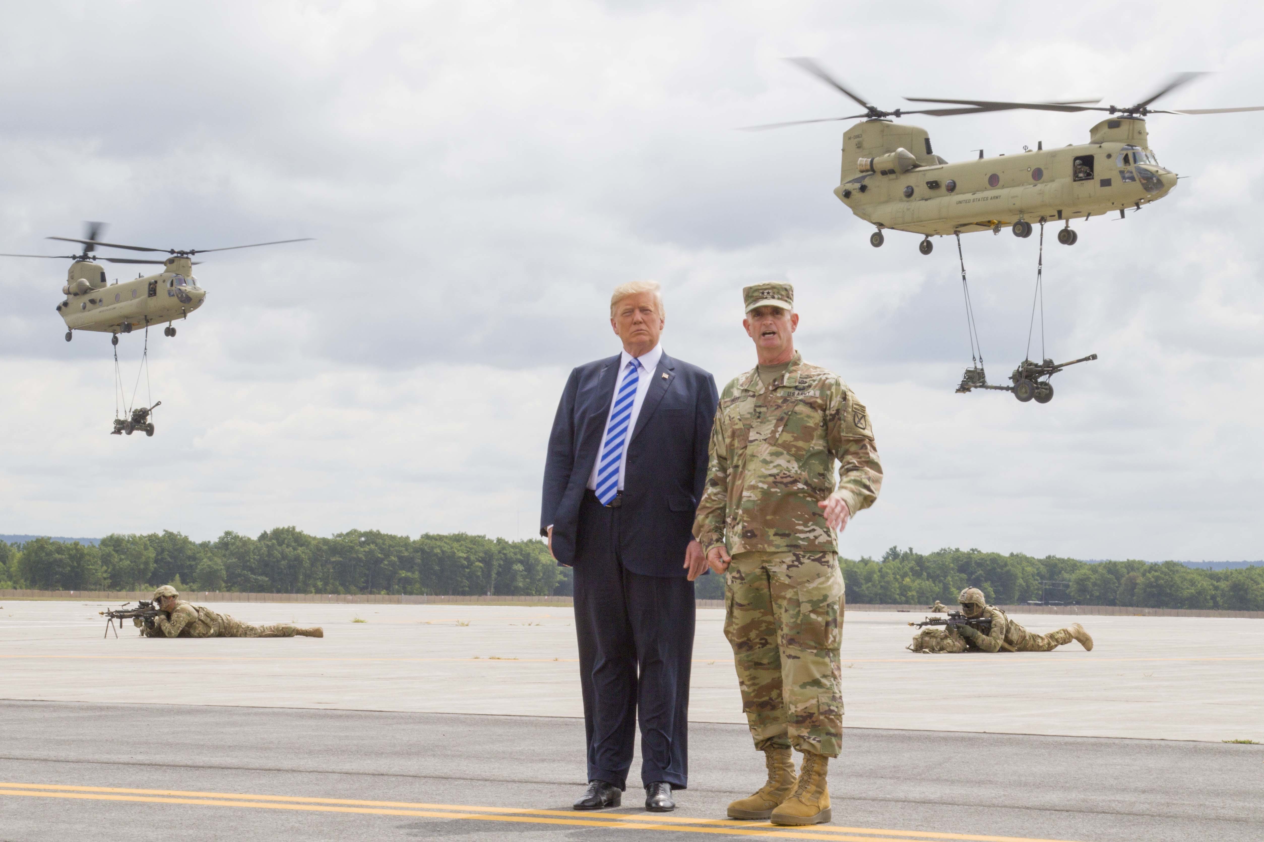President Donald J. Trump and Maj. Gen. Walter E. Piatt, commander of the 10th Mountain Division (LI), look on as CH-47 Chinook helicopters carry in artillery during a demonstration at Fort Drum, New York, Aug 13 CREDIT DVIDS