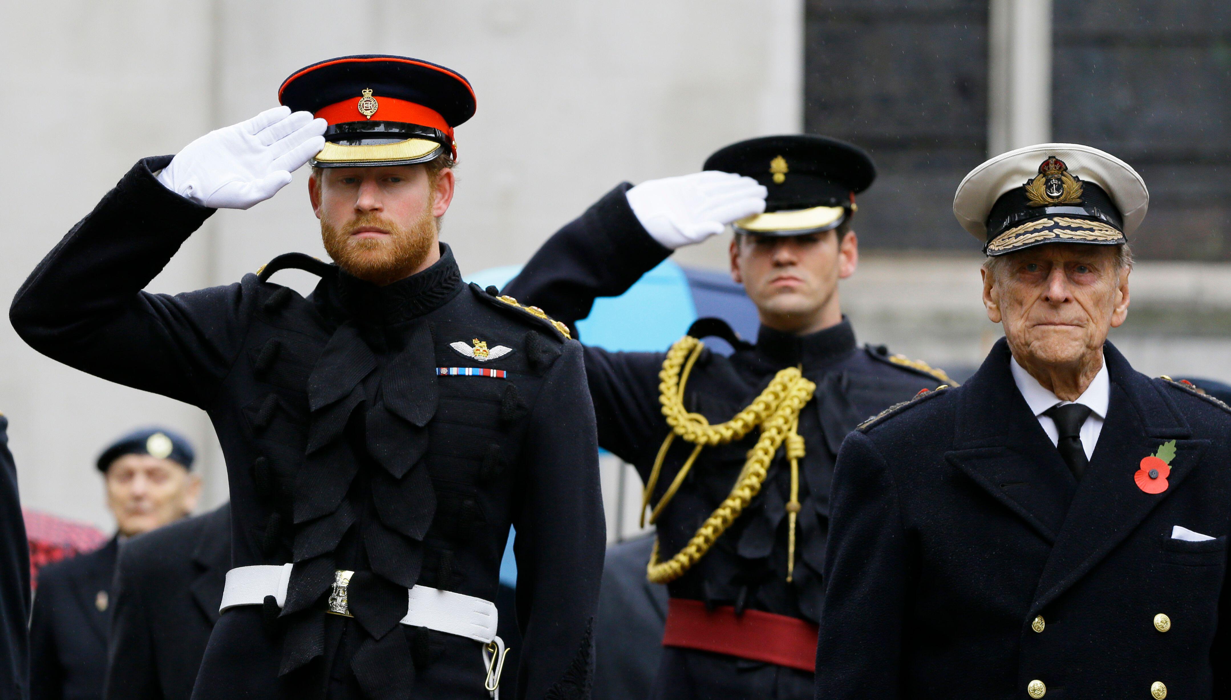 Prince Harry salutes as he stands alongside Prince Philip during a visit to the Field of Remembrance at Westminster Abbey in London