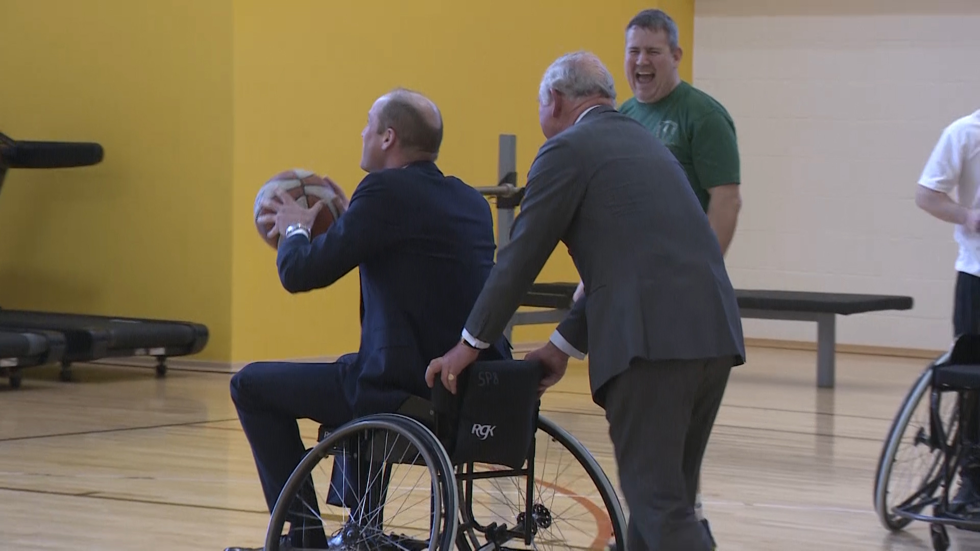 Prince William tries a spot of wheelchair basketball with the help of his father.