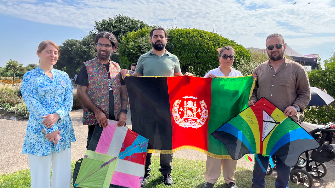 (L-R) Dewa Khan, Sanjar Qiam, Maiwand Mohmand and Horia Mosadiq with her husband Zamarey Faqiri standing with their kites and flag on Blackburn beach.