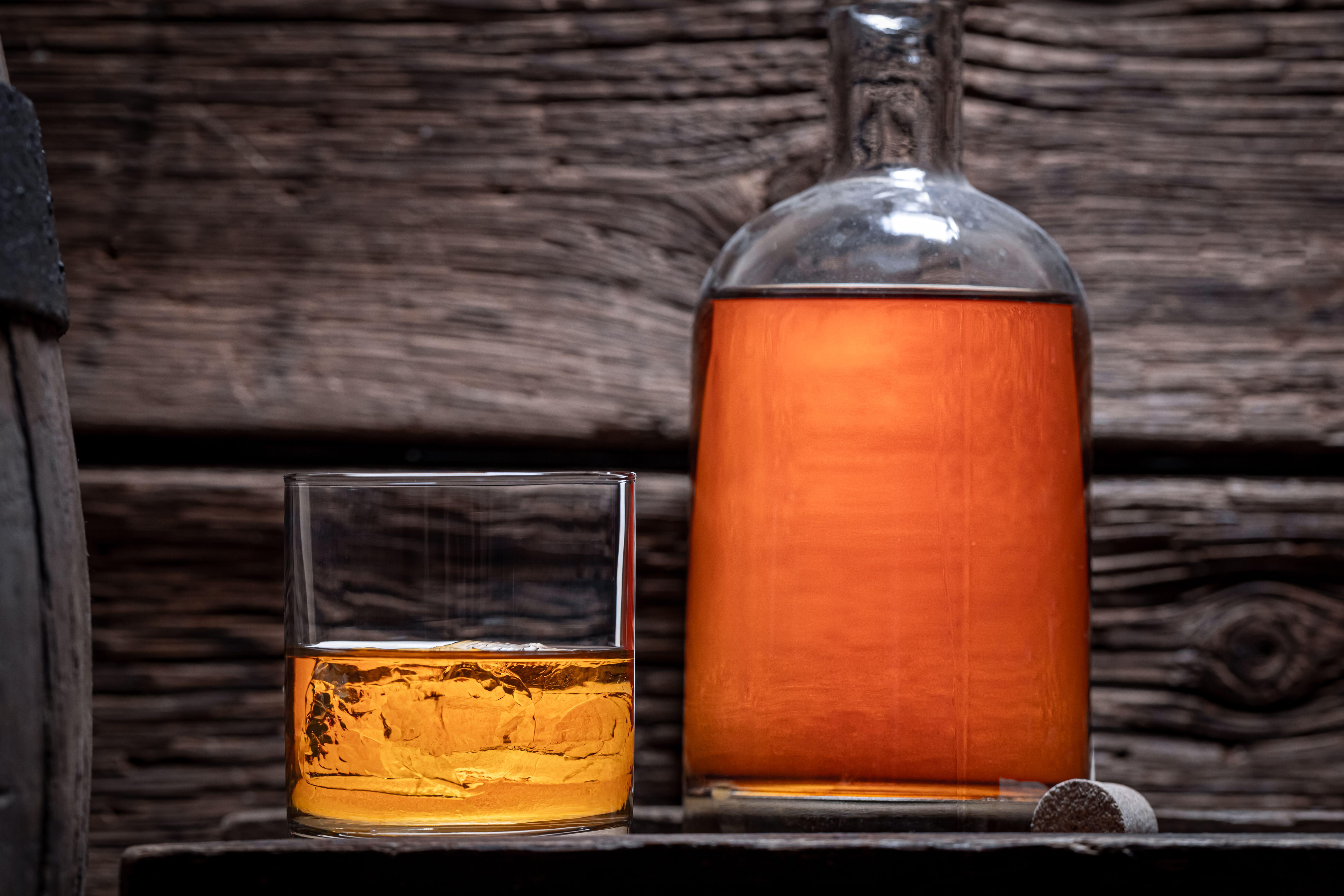 Image ID: 2HXH5MF: Good cognac with bottle in old wooden distillery. Glass of bourbon with ice in an old distillery (Picture: Jacek Nowak / Alamy Stock Photo).