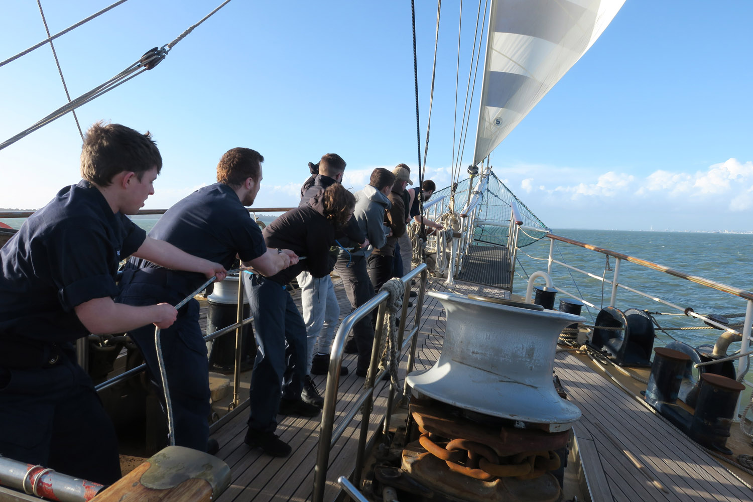 Sailors and ships company haul in a line on TS Tenacious
