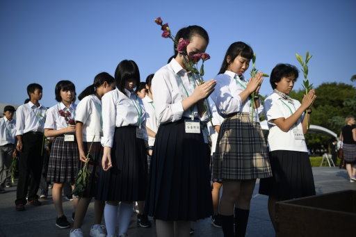 Visitors lays flowers and pray for the atomic bomb victims in front of the cenotaph (Picture: PA).