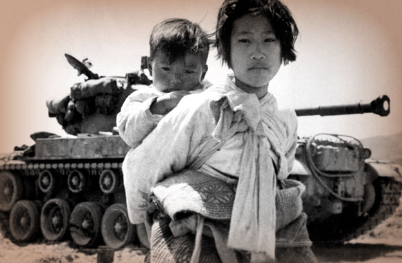 With her brother on her back a war weary Korean girl tiredly trudges by a stalled M-26 tank in Haengju, Korea, June 9, 1951