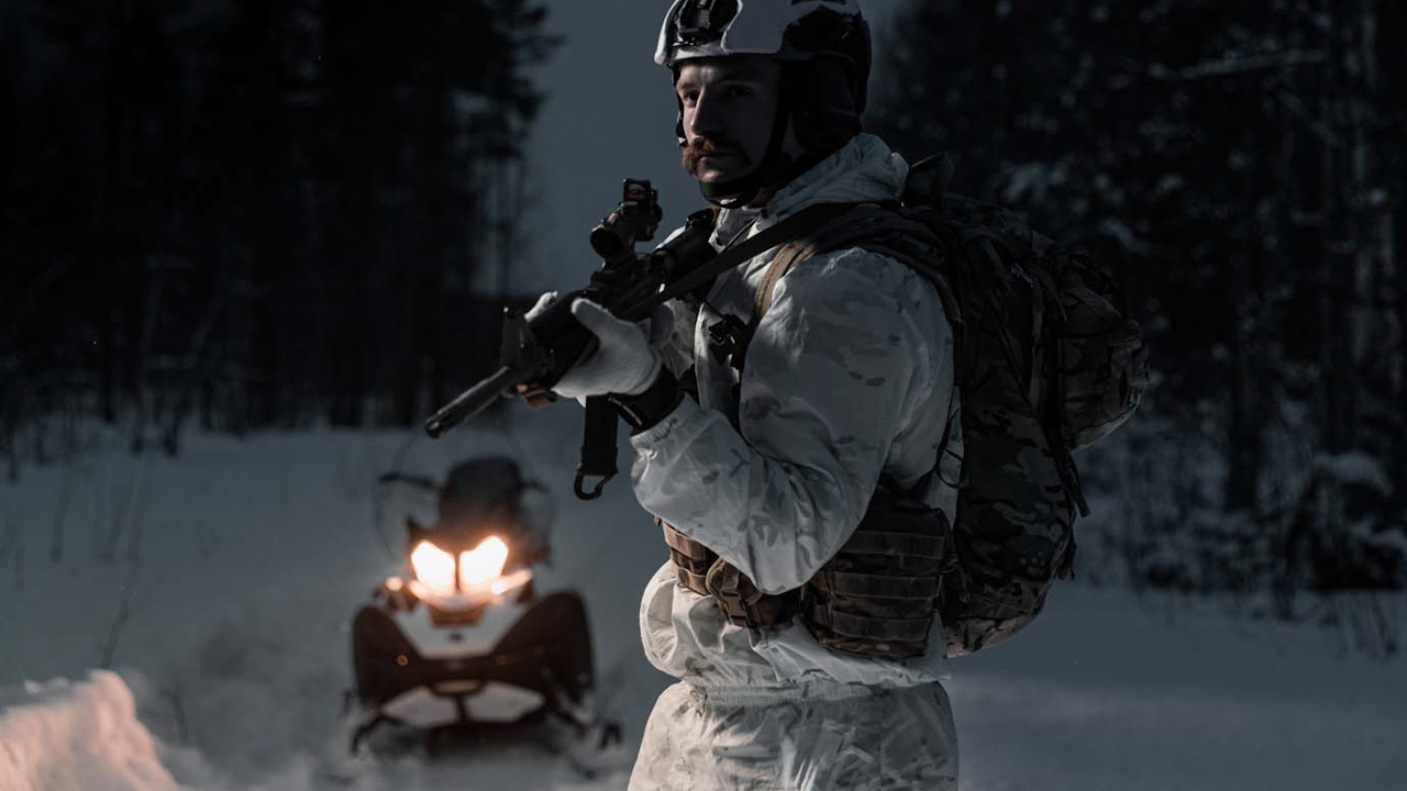 A Royal Marine from 45 Commando stood with his weapon and the Over Snow Reconnaissance Vehicles (Picture: Royal Navy).