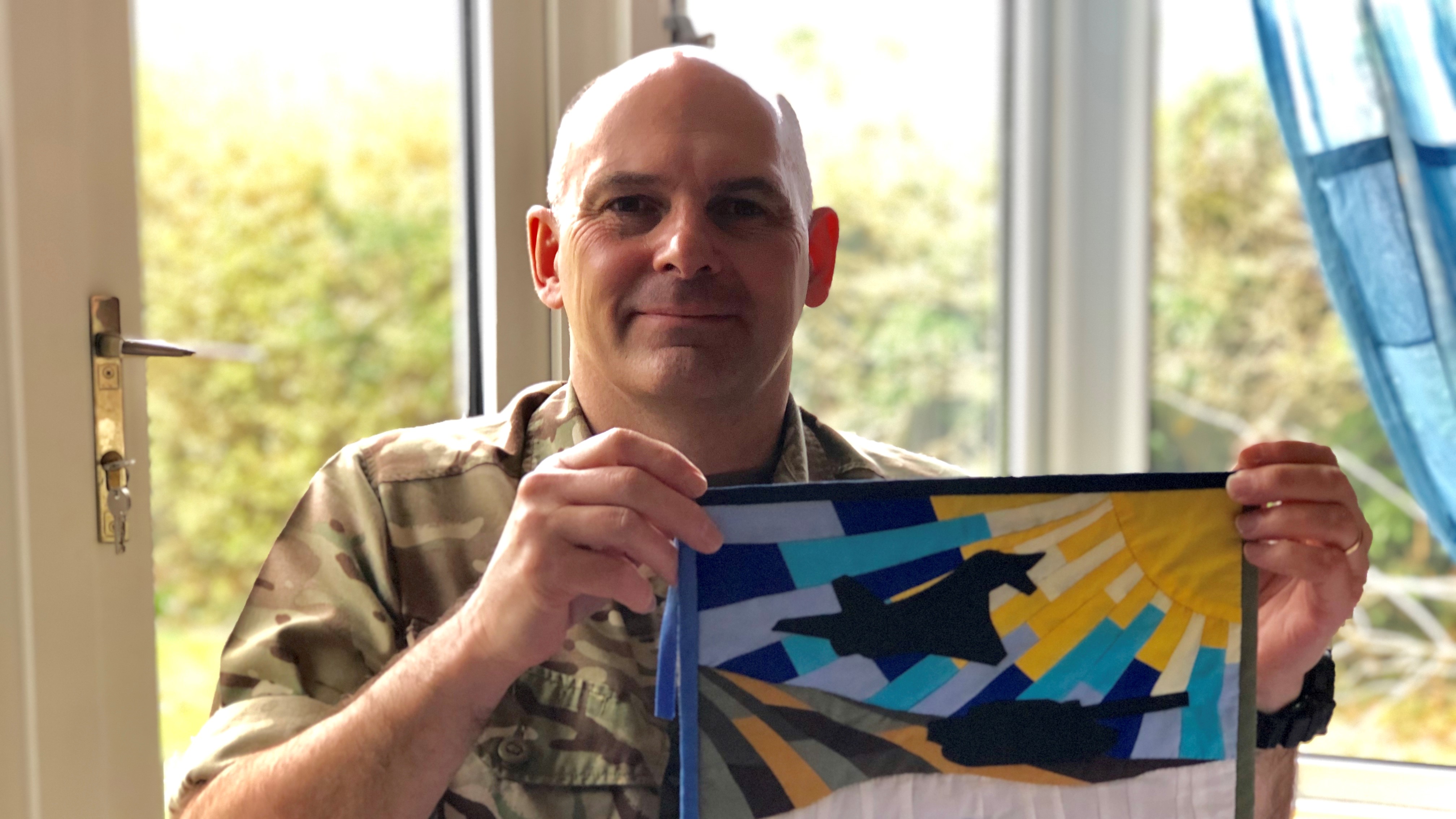 "Sewing Soldier" Neil Stace, holding up a flag he has sewn