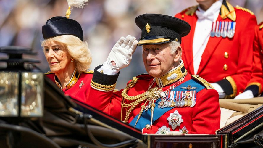 King Charles returns the salute while being driven down The Mall in his carriage - Queen Camilla's Grenadier Guards ensemble was made for her specially for the occasion