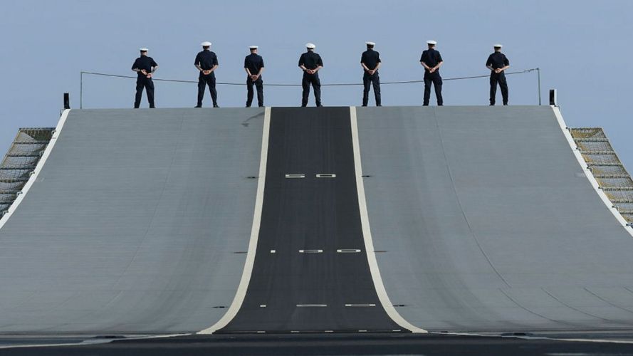Sailors line up at the top of the flight ramp on HMS Prince of Wales as she sails into Portsmouth Harbour at the end of Phase 1 of Operation Firecrest