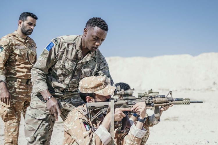 A member of 16 Air Assualt Brigade training a Kuwaiti counterpart, aiming a weapon, on Exercise Desert Warrior 