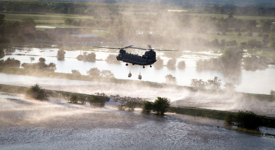 Chinook helicopter lowers bag of aggregates into the breach of a riverbank in an effort to stop the river Steeping causing further flooding to the local area CREDIT RAF