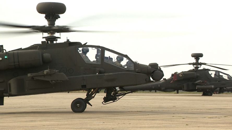 Two Apache AH-64E helicopters sit on the apron side by side.