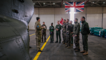 French and British personnel in a hanger with British flag in the background