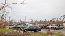 A car park where most cars have suffered some form of damage. Fallen branches and broken buildings become airborne projectiles in the hurricane winds.