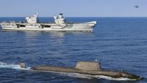 HMS Queen Elizabeth (background) with an Astute Class submarine and Merlin helicopter on Carrier Strike Group 21 deployment (Picture: MOD).