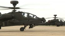 Two Apache AH-64E helicopters sit on the apron side by side.