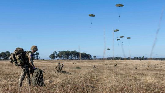 A soldier, with his bergen already on his back, packs away his parachute after landing on the drop zone