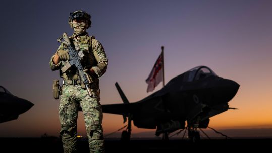 A Royal Marines Commando armed with a Sig Sauer MCX rifle stands guard on the flight deck of HMS Prince of Wales as she transits the Suez Canal