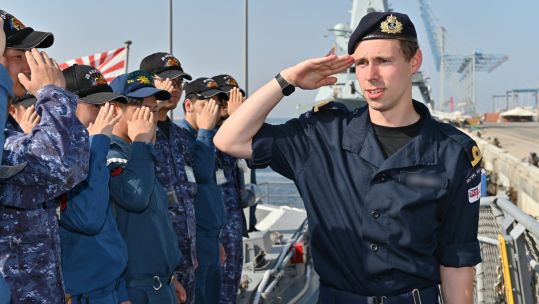 A member of the Royal Navy salutes the JMSDF as he walks down a line of JMSDF personnel (Picture: JMSDF X)