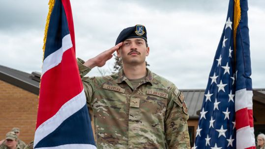 A US airman salutes the flags of the United Kingdom and the United States at RAF Fairford in Gloucestershire (Picture: US Department of War)