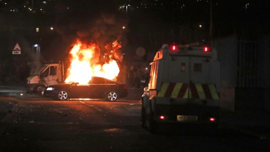 A burning car in Creggan, Londonderry, after petrol bombs were thrown at police during riots (Picture: PA).