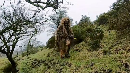 A trainee British Army sniper camouflaged against a natural backdrop