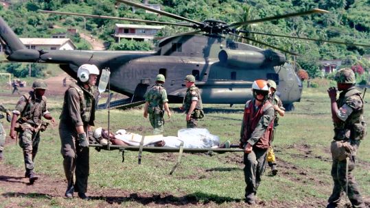 Photograph of casualties on stretchers during US invasion of Grenada in 1983 with helicopter in background