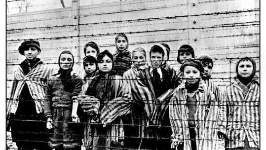 Child prisoners wearing striped uniforms stare out from behind a barbed wire fence in notorious WW2 Nazi death-camp Auschwitz Southern Poland Holocaust (Picture: Shawshots / Alamy Stock Photo).