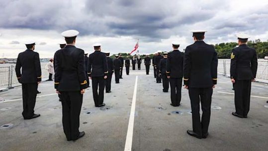 Crew members look on at the White Ensign which was raised from the ship's deck for the first time (Picture: Royal Navy).