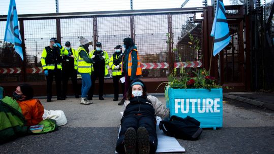 Cover image: Extinction Rebellion protestors outside the base earlier on Friday (Picture: PA Images/Alamy Stock Photo).