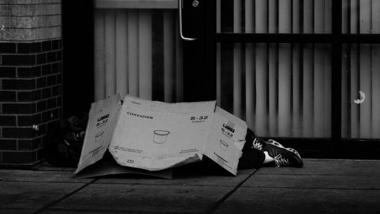 Homeless person with cardboard SOURCE The Collab - Pexels
