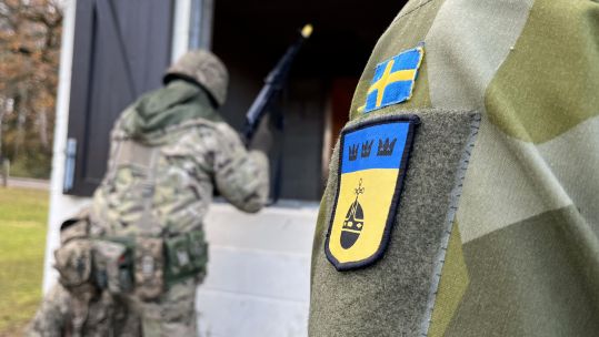Looking at a Ukrainian badge on the uniform of a volunteer in a fake UK village for frontline training 301123 CREDIT BFBS.jpg	