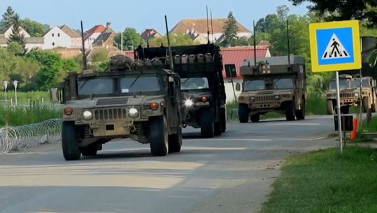 NATO vehicles move down a road in Europe.