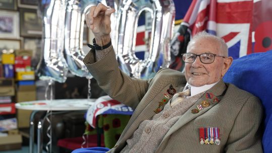 Cover image: Tommy Trotter with '100' balloons behind him (Picture: PA).