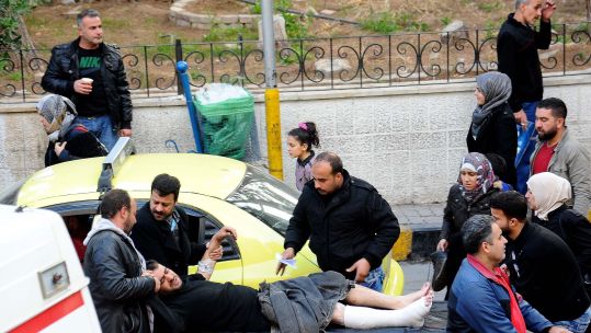 People get a wounded man into ambulance in Damascus, capital of Syria. CREDIT PA