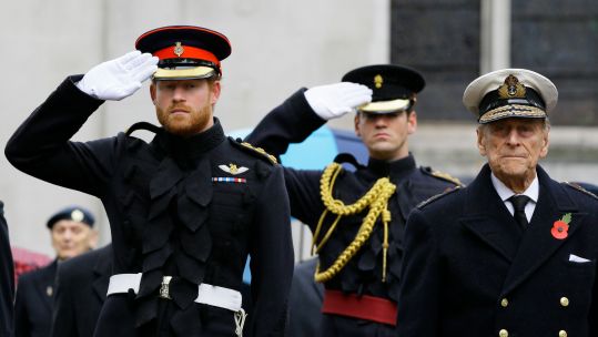 Prince Harry salutes as he stands alongside Prince Philip during a visit to the Field of Remembrance at Westminster Abbey in London